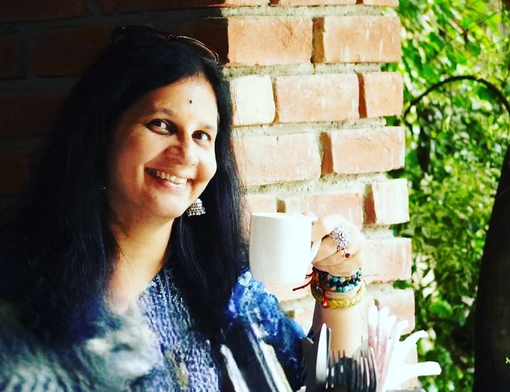The founder of Garam Dibba smiling with a cup of tea against a brick wall