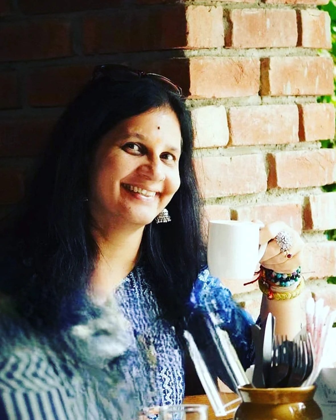 The founder of Garam Dibba smiling with a cup of tea against a brick wall
